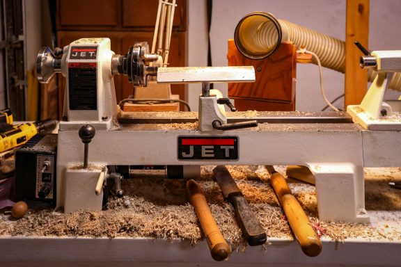 A wood lathe with tools and wood shavings on a workbench.